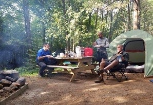 3 men at a camp site sitting at a picnic table